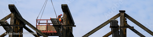 Foto Workman in safety equipment in work basket help aloft by crane, old wood railway