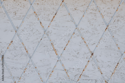 Rusty metal lattice with diamond pattern in front of a white textured wood panel