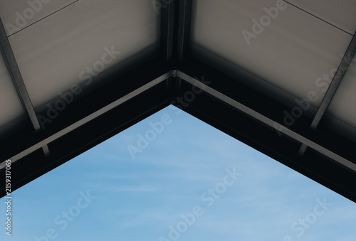 Low angle view of symmetrical geometric roof structure framing blue sky