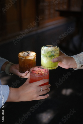 Two people clinking colorful layered cocktails in trendy bar setting at night