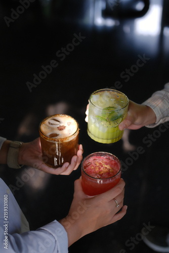 Close-up of hands clinking colorful layered cocktails in stylish glasses at night event