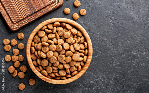 Top View of Dry Pet Food Kibble in a Wooden Bowl on a Dark Textured Surface