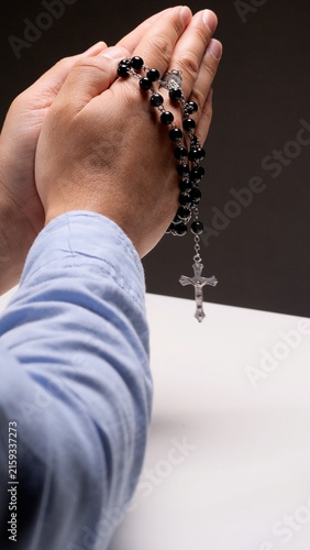 Fotografía Hands clasped together in prayer, holding a black rosary with a silver crucifix,