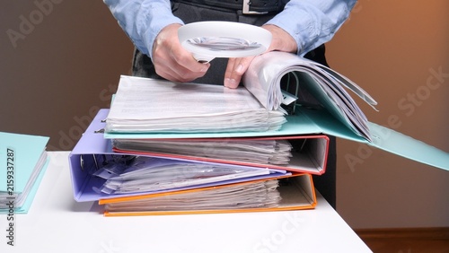 Konstfotografi Man in a blue shirt carefully examining financial papers in a binder with a magn