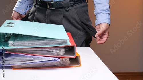 Bild auf Leinwand Person standing behind a stack of binders and documents, turning out pants pocke