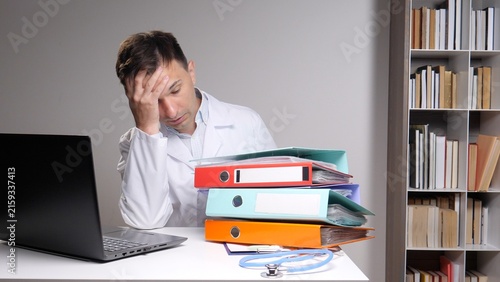 Foto Exhausted healthcare professional sitting at a desk with a laptop and a large st