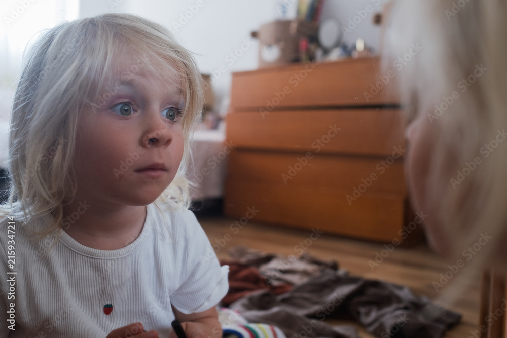 Fototapeta premium Little Girl Looking Surprised in a Mirror Indoors