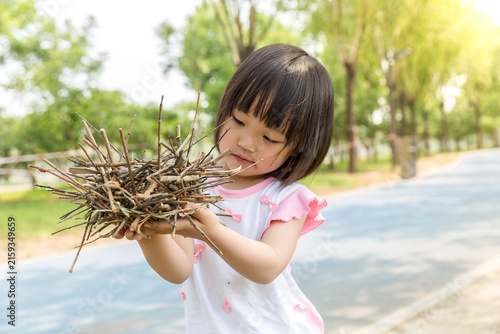 Fotografie Curious Little Girl Holding a Nest of Dry Branches and Sticks in the Park, Natur
