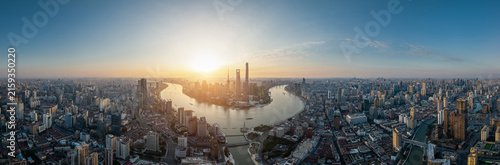 Aerial panoramic shot of a dense urban skyline curving river under bright sunrise light, showcasing modern architecture.