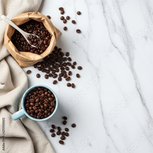 Premium roasted coffee beans spill out from a rustic paper bag next to a light blue ceramic mug on a luxury white marble surface, perfect for cafe branding and promoting organic morning energy drink.