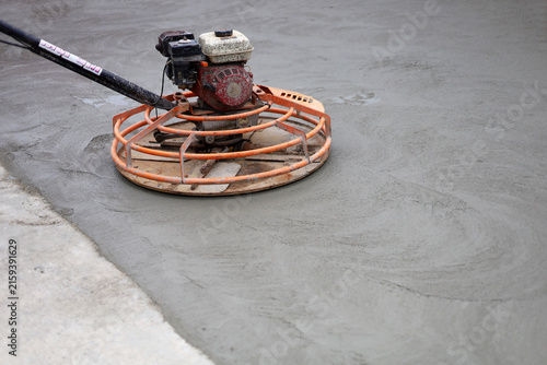 An orange power trowel machine finishing a fresh wet concrete surface on a road construction site.