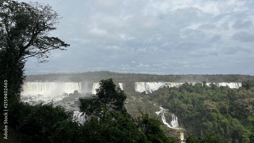 Fototapeta premium Majestic Iguazu Falls in Brazil showcasing powerful cascades amidst lush green rainforest under a cloudy sky