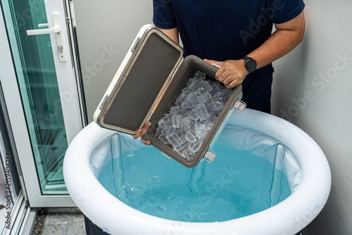 Pouring ice cubes into inflatable tub for ice bathing, practicing cold therapy and Wim Hof Method for wellness meditation fitness recovery and sports therapy.