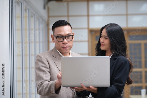 Professional mentor showing digital strategy to female employee on notebook. Successful Asian business partners collaborating on computer project in office. Dedicated office workers looking at screen.