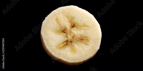 A single slice of ripe banana with visible seeds rests on a dark surface