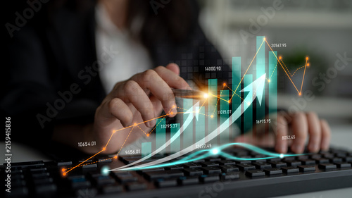 A business professional uses a keyboard while examining financial data. The image showcases digital graphs and charts symbolizing growth and market analysis trends. Scalp