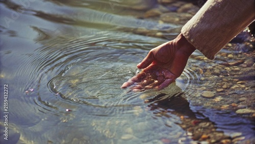 Person touching clear river water creating ripples in sunny nature stream