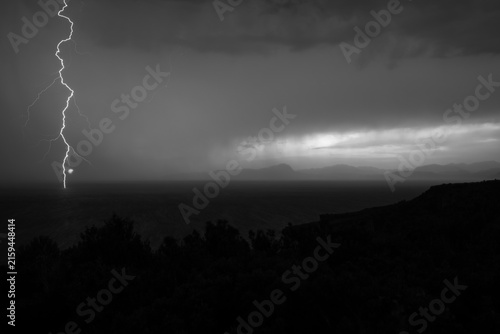 black and white dramatic lightning strike over ocean with stormy cloudy sky and distant mountains silhouette