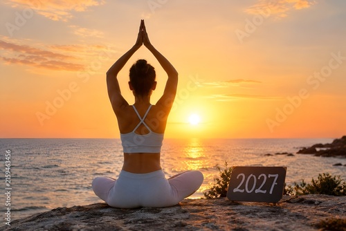 Woman practicing yoga at sunset with 2027 sign for new year wellness and mindfulness goals