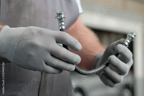 Car service.The car’s braking system.The auto mechanic has a new brake hose in his hands.Checking the proper condition of the new part, preparing for installation.