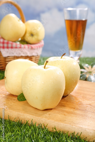 Fresh Golden Apples on Wooden Board with Basket and Juice Glass in Garden Setting