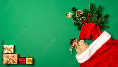 Santa Claus suit with holiday gift boxes and fir branches on green background with copy space