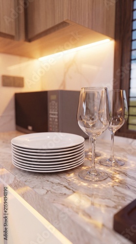 Stack of white ceramic plates and two empty wine glasses on a modern marble kitchen countertop