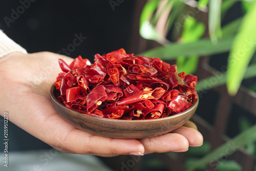 Принти на полотні Dried Red Chili Pepper Flakes in Wooden Bowl Held by Hands - Spicy Cooking Ingre
