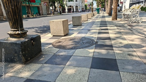 A clean sidewalk with concrete cubes along the edge for seating and protection from cars.