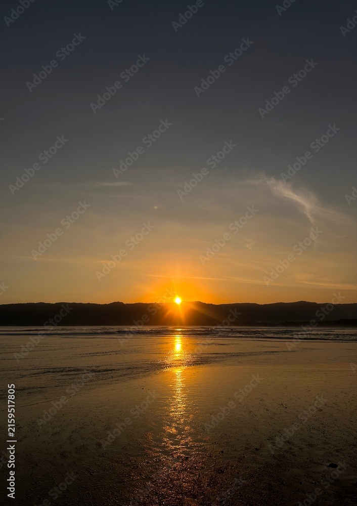 Obraz premium Golden Sunset Over Tropical Beach with Sunlight Reflection on Wet Sand