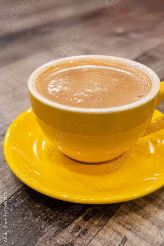 Foto Traditional Malaysian teh tarik, a creamy and frothy pulled milk tea served in a bright yellow ceramic cup and saucer on a rustic wooden table