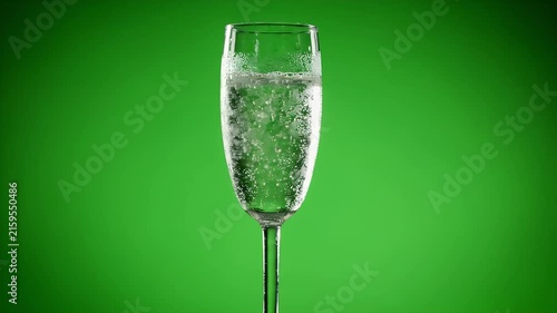 A single glass of sparkling water or champagne with bubbles against a vibrant green background, perfect for advertising or lifestyle content