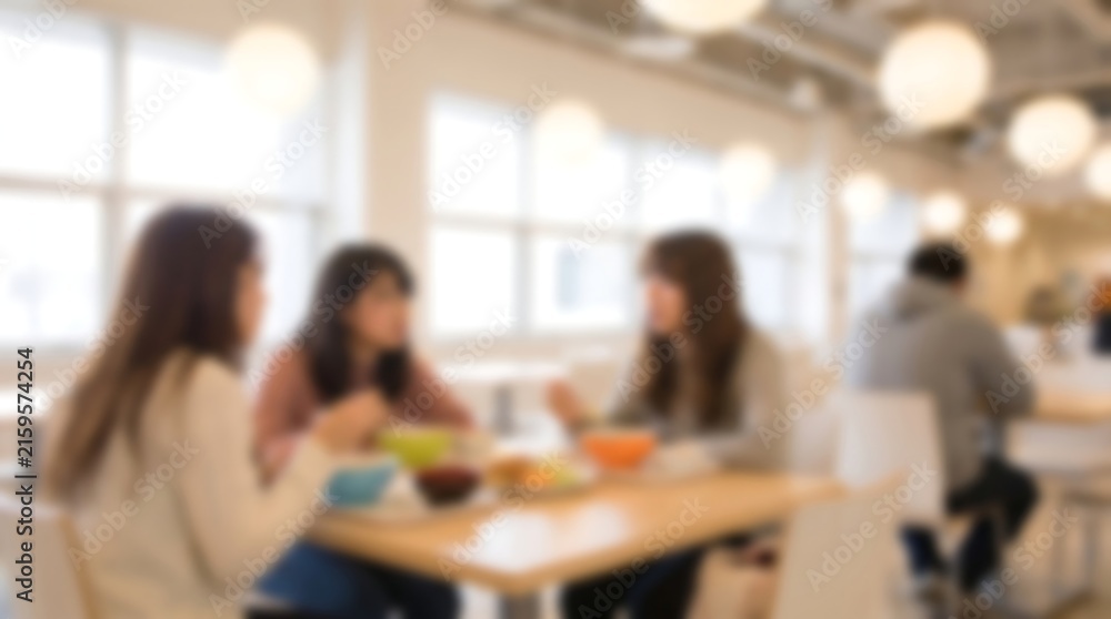 Obraz premium Blurred group of colleagues chatting during lunch break in modern bright office cafeteria with large windows and comfortable seating while enjoying meal and conversation together