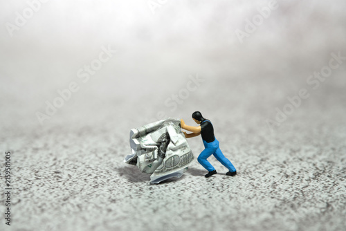 Miniature people figure toys photography. A man worker pushing a squeezed of money on the floor