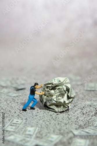 Miniature people figure toys photography. A man worker pushing a squeezed of money on the floor