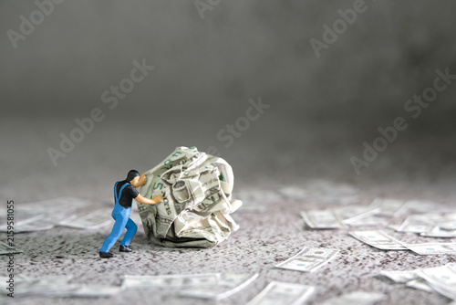 Miniature people figure toys photography. A man worker pushing a squeezed of money on the floor
