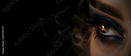 Macro close up of beautiful female eye with dark smokey eyes makeup and burning candle reflection in pupil, luxury gothic cosmetics and dark moody conceptual fine art with large copy space