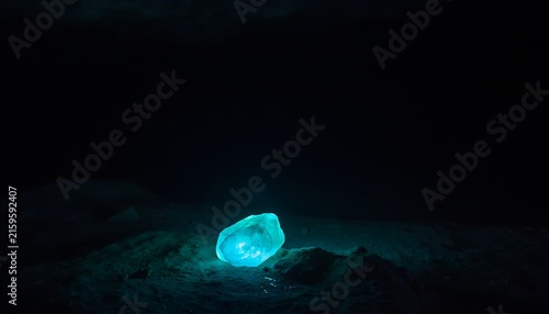 Glowing blue crystal in dark cave, luminous magic gemstone on cavern floor, mysterious radiant mineral in underground grotto