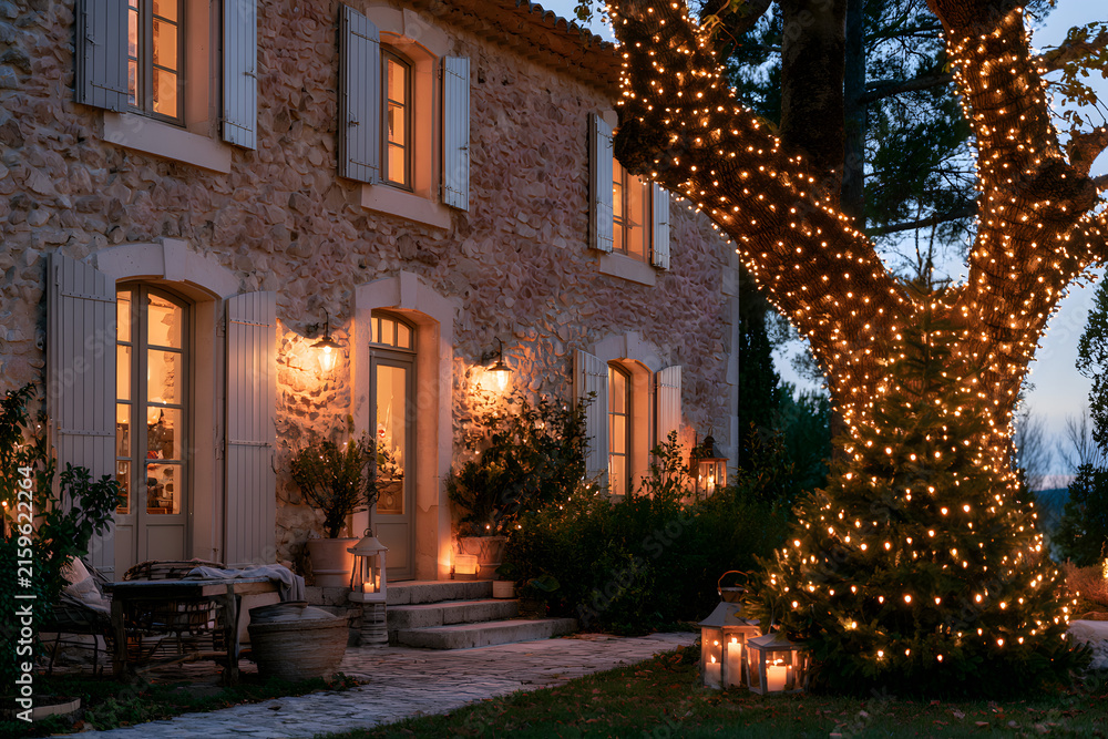 Fototapeta premium Charming Provençal Farmhouse Exterior Decorated with Festive Lights for a Cozy Night Setting