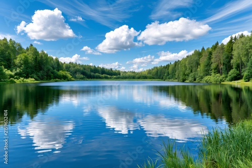 Calm forest lake reflecting blue sky and clouds