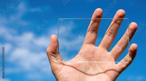 Transparent Rectangle Held by Hand Against Bright Blue Sky and Clouds