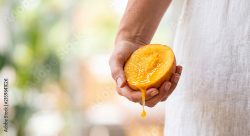 Woman Holding a Half Sliced Ripe Mango with Juice Dripping Down