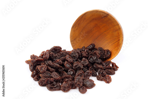 Dried dark raisins spilling out of a wooden bowl isolated on white background.