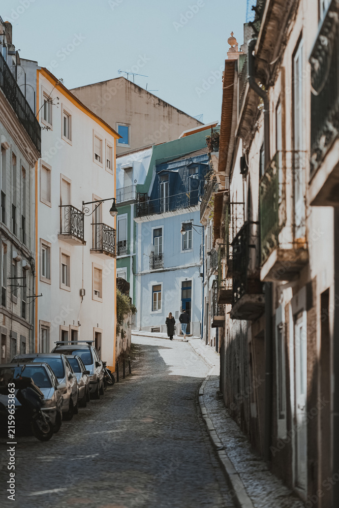 Fototapeta premium People walking up a narrow cobblestone street in Lisbon