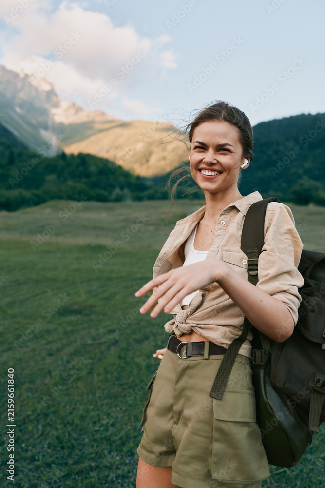 Naklejka premium Young woman hikes through a sunlit mountain meadow with a backpack, smiling as she explores a rugged trail, embracing nature and adventure today, freedom.