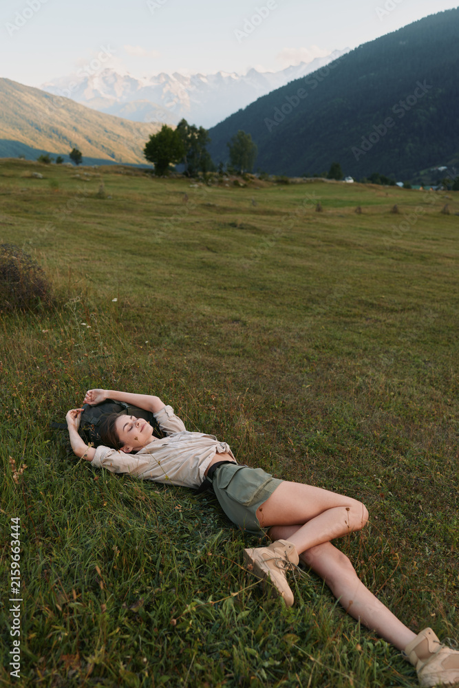 Naklejka premium Relaxed woman lies on a grassy meadow in a wide field, enjoying outdoor lifestyle under warm sun, casual pose and peaceful nature vibes in a rural landscape