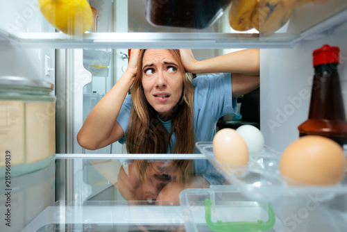 фотографія Shocked Woman Looking In Refrigerator Finding Nearly Empty Shelves In The Morning