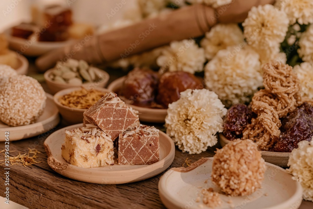 Fototapeta premium Traditional Indian sweets on a rustic red wooden table, featuring sticky syrups and crumbly textures for a festival food catalogue