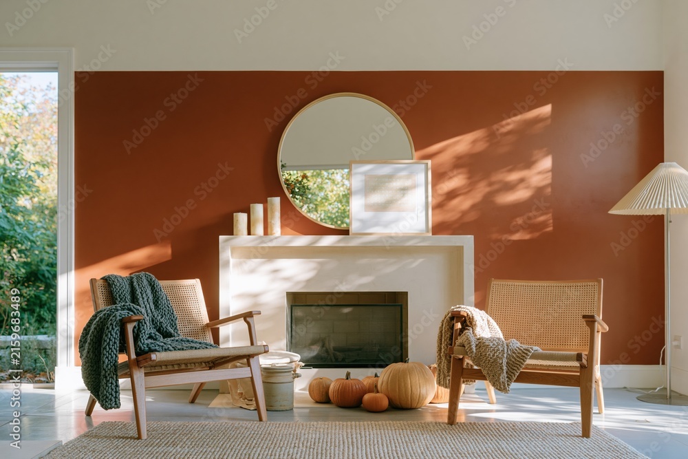 Fototapeta premium Terracotta orange wall in a cozy autumn living room with woven armchairs and a fireplace for home staging and interior design retail