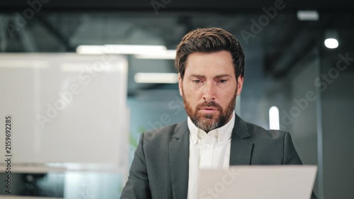 Businessman reviews important document, expressing growing stress, concern. Problems require careful consideration, focused attention in office environment.
